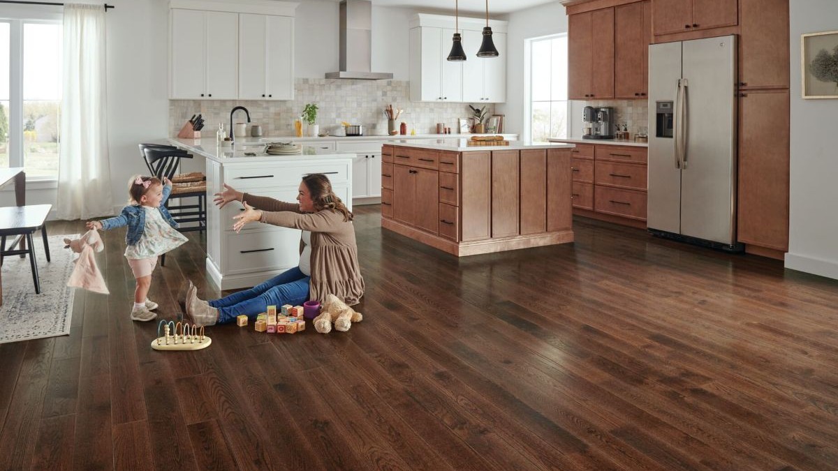 Mother playing with infant child on the kitchen floor featuring real hardwood flooring